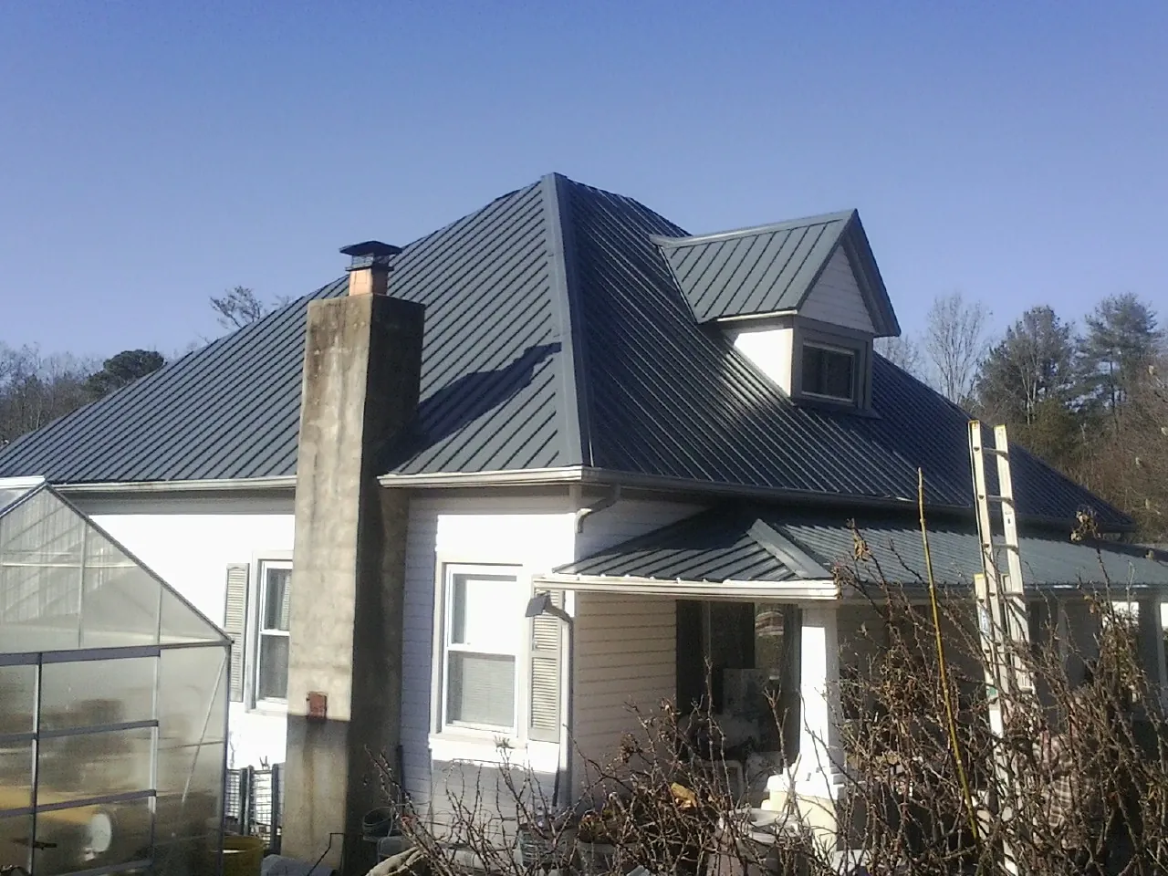 Dark blue standing seam metal roof on a white farmhouse with dormer — Slate & Tile Roof Repair by Roofing Brothers in Rock Creek