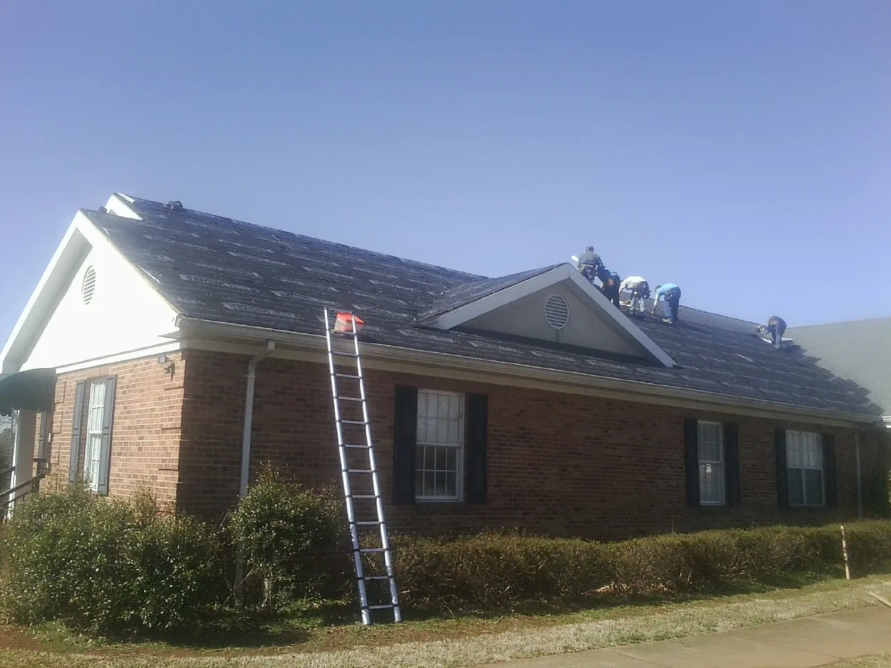 Crew tearing shingles off a brick ranch roof with a ladder set — Metal Roof Repair work by our crew in Rock Creek