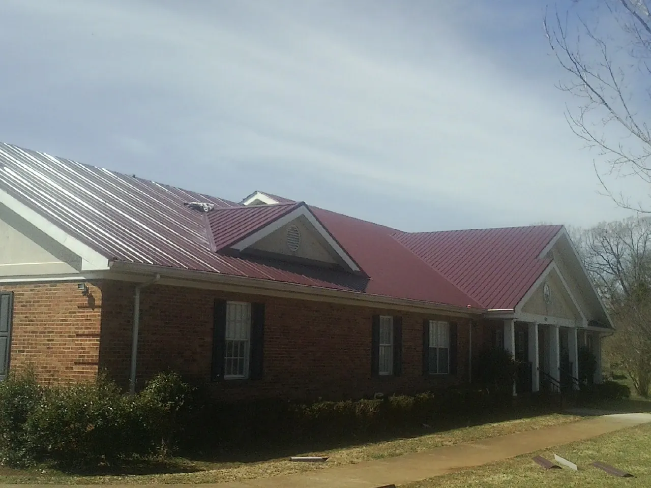 Red metal roof with gabled entries on a long brick building, from a Hail Damage Roof Repair job in Rock Creek