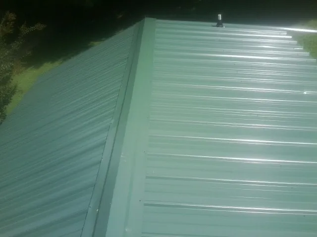 New green metal panels meeting at the ridge of a roof — Flat Roof Repair work by our crew in Rock Creek