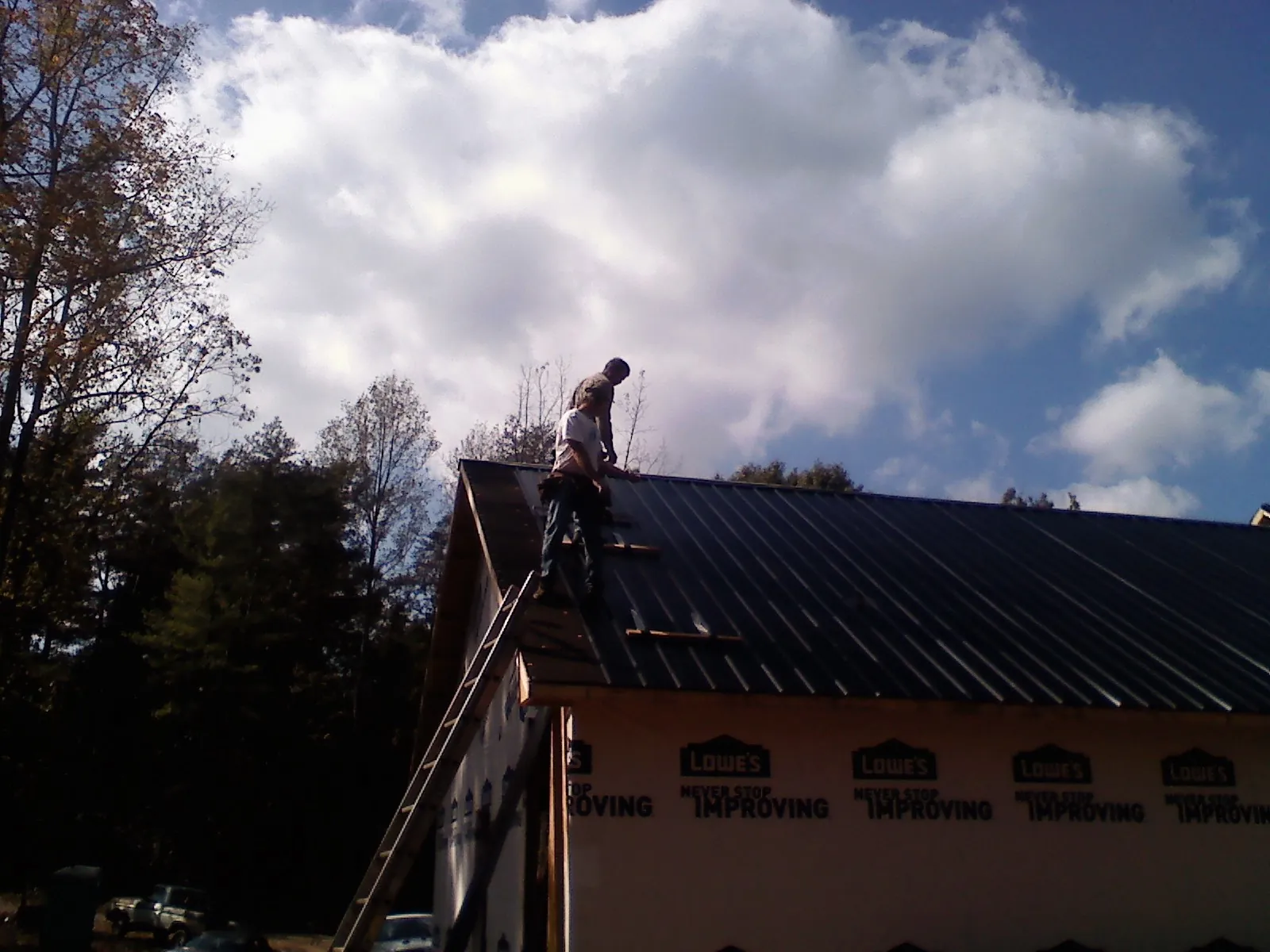 Roofer fastening dark metal panels high against a cloudy sky, from a Roof Inspection job in Rock Creek