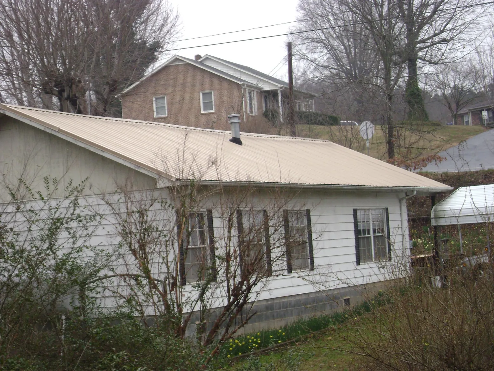 Tan metal roof on a white sided house set into a hillside — Commercial Roofing by Roofing Brothers in Rock Creek